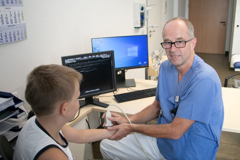 Dr. Ulrich Altrup untersucht den Arm eines jungen Patienten per Ultraschall