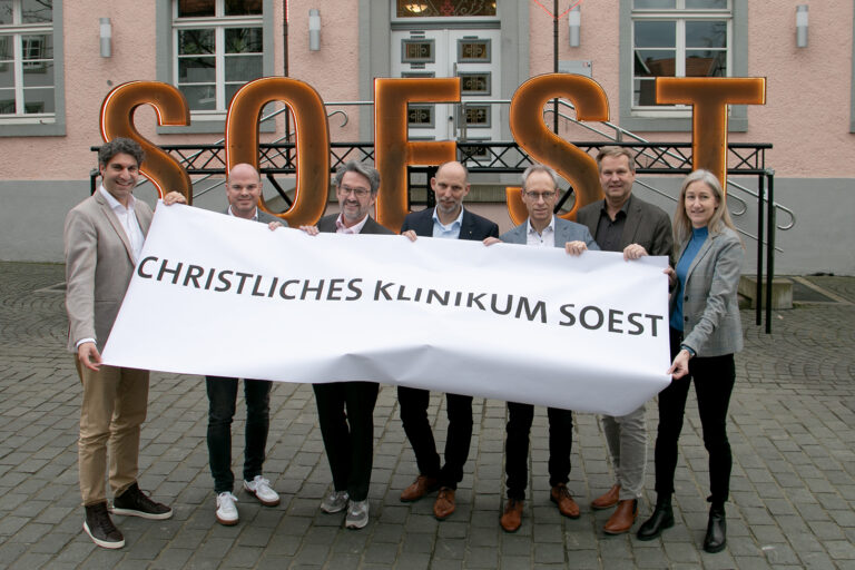 Das Bild zeigt (v.l.): Christan Schug (Geschäftsführer KlinikumStadtSoest), Tobias Franke (Kfm. Direktor Marienkrankenhaus Soest), Dr. Eckhard Ruthemeyer (Bürgermeister Stadt Soest), Christian Larisch (Geschäftsführer Hospitalverbund), Guido Ponto (Vorsitzender Verwaltungsrat Hospitalverbund), Thorsten Roy (Geschäftsführer Christliches Klinikum Unna) und Sabine Boschert (Kfm. Direktorin KlinikumStadtSoest). Sie halten gemeinsam ein Banner mit der Aufschrift "Christliches Klinikum Soest".